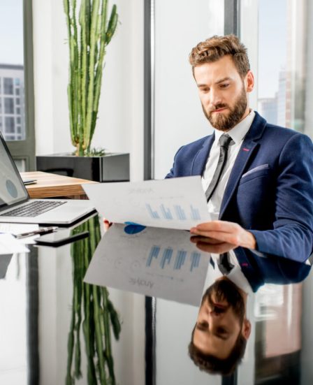 Handsome analytic manager working with paper charts and laptop at the luxury office interior